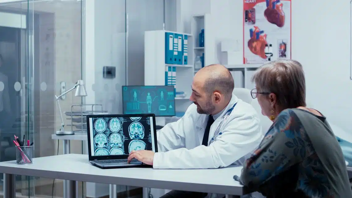 En la oficina de los médicos hablando de escáneres cerebrales, tomografía computarizada, resonancia magnética y la exploración de rayos X en la pantalla del ordenador portátil para el paciente mujer mayor. Diagnóstico cerebral, imagen médica CT, MRI o X Ray resultados en moderno hospital privado o clínica. Radiólogo radiología sistema sanitario
