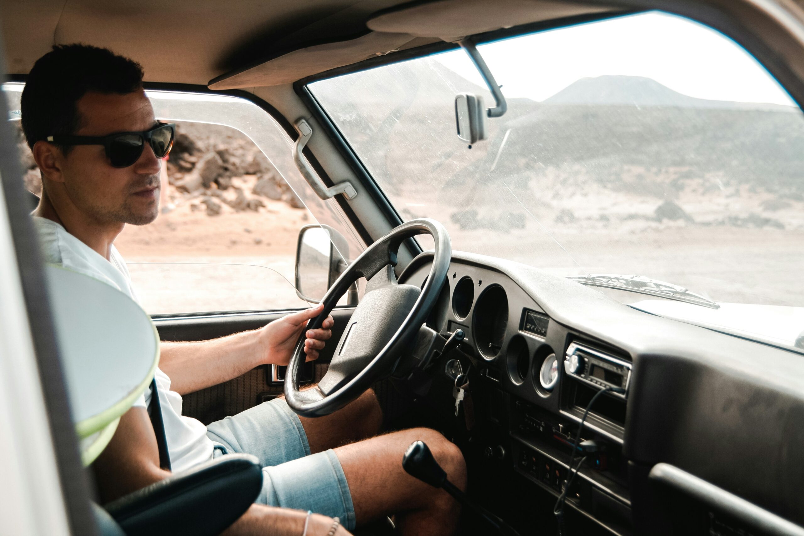 A man wearing sunglasses is driving a car, focused on the road ahead.