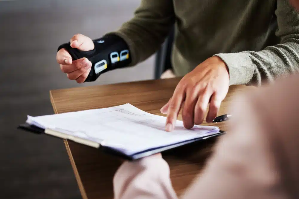A man wearing a wrist brace consults with a woman holding a pen, discussing personal injury legal matters.